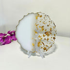 Decorative plate with gold flakes on a stand, next to purple flowers.