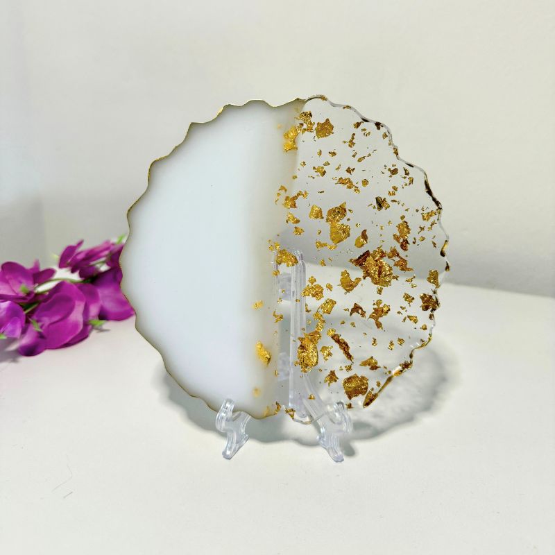 Decorative plate with gold flakes on a stand, next to purple flowers.